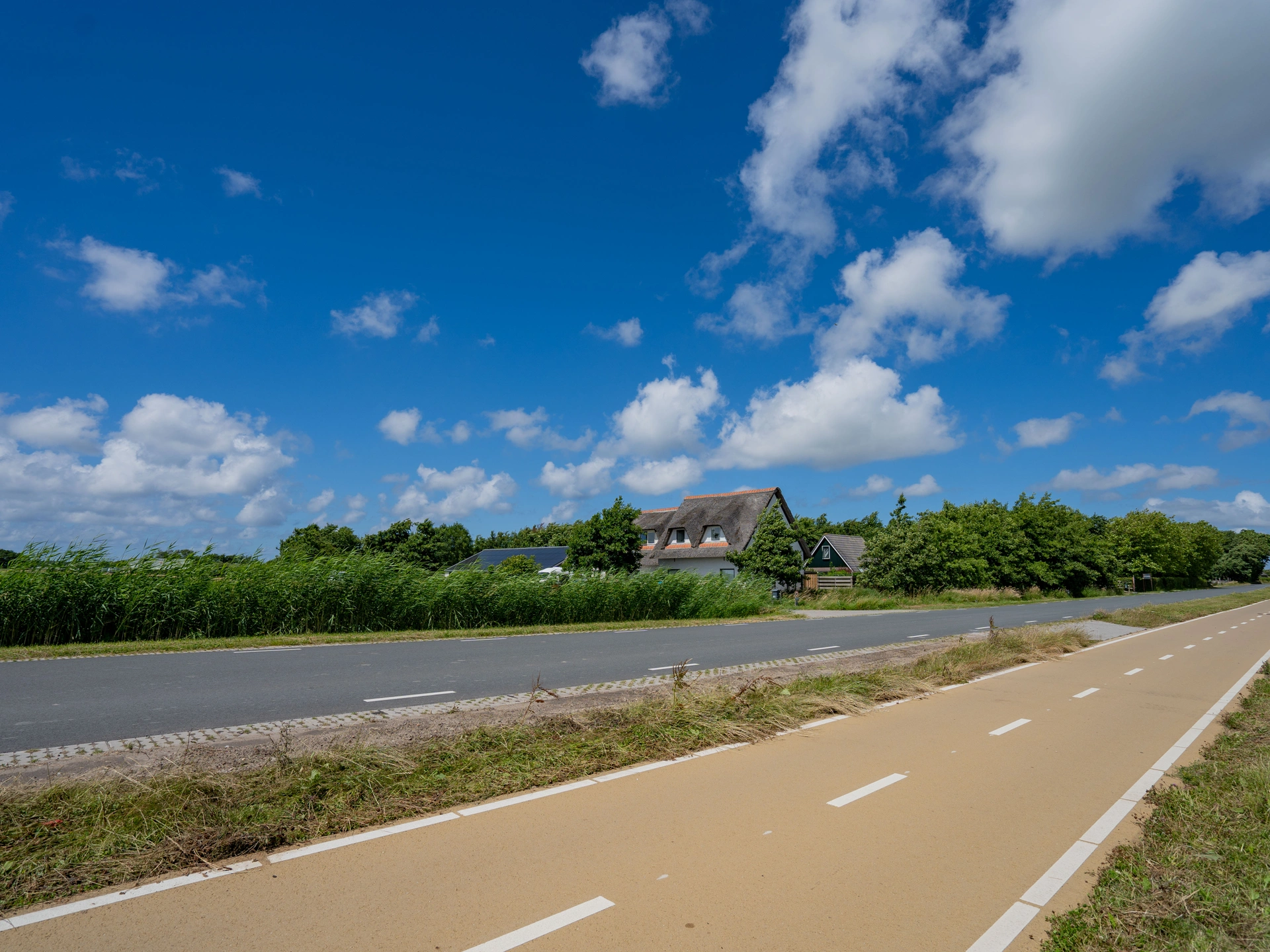 Fietspad langs de weg met in de verte de rieten daken van Huize Goethe onder een blauwe lucht