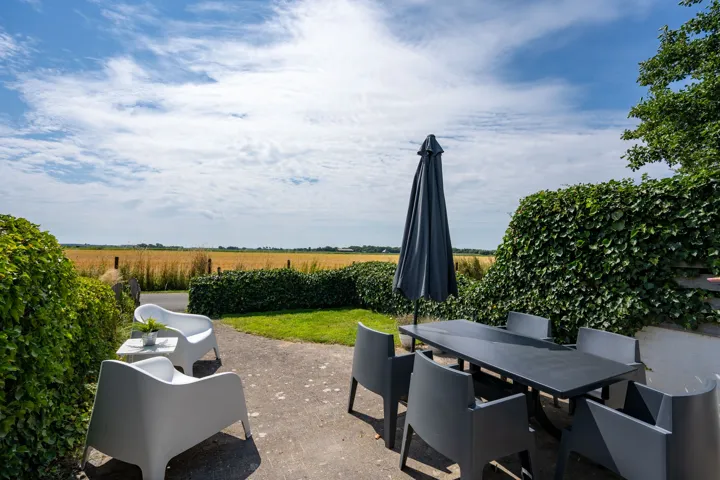 Terras met eettafel, loungestoelen en parasol, met vrij uitzicht over de velden